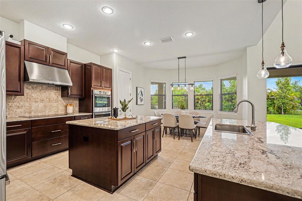 A kitchen with dark wood cabinets, granite countertops, a center island, and a dining area — 14903 OLD TOM MORRIS COURT, TAMPA, FL