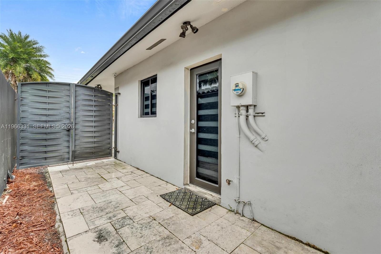 An exterior view shows a paved patio, a gray door, a window, and a gate — 344 NW 136th Pl # B, Miami FL 33182, MIAMI, FL