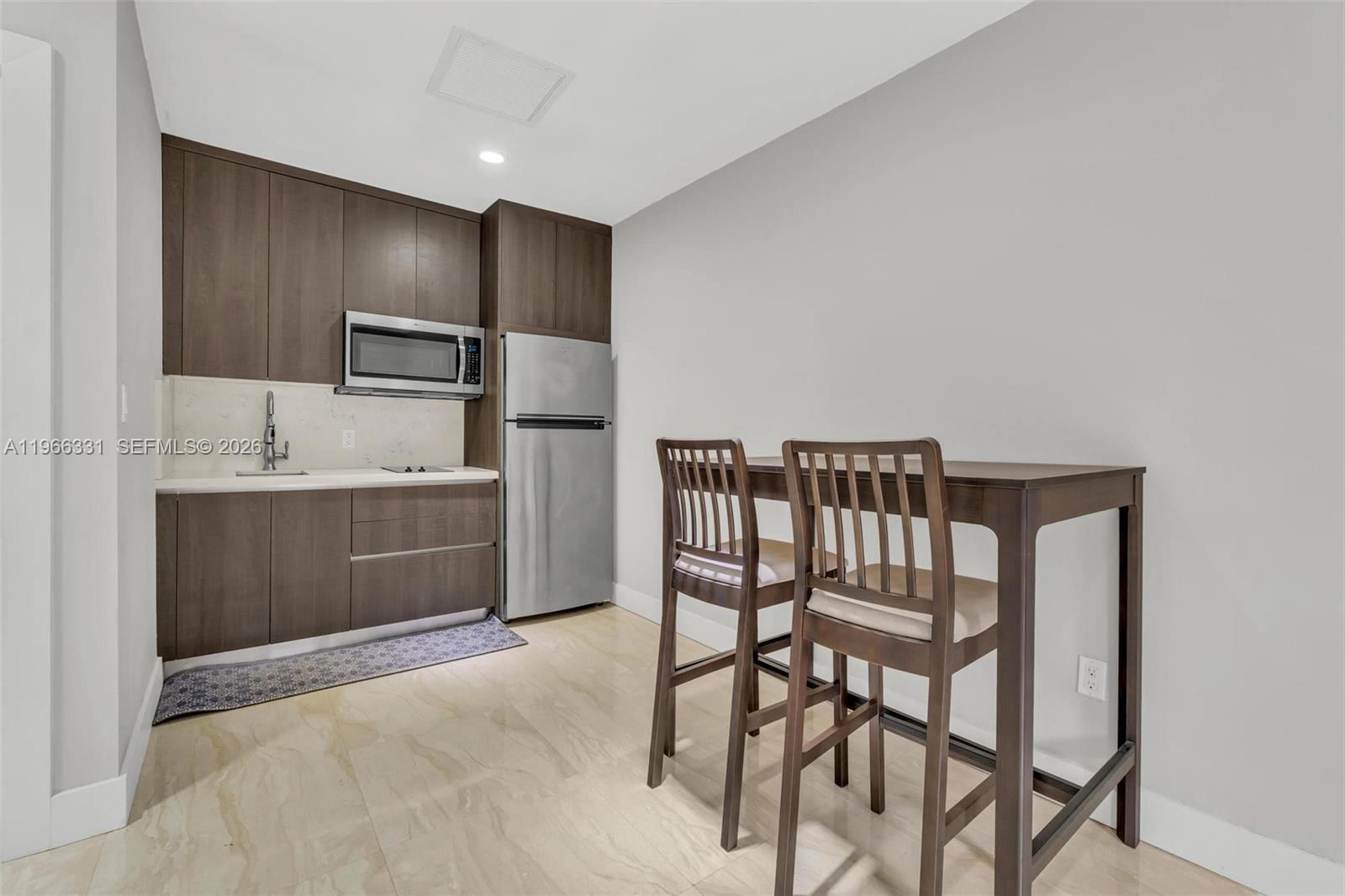 A small kitchen features dark wood cabinetry, stainless steel appliances, and a high-top dining table — 344 NW 136th Pl # B, Miami FL 33182, MIAMI, FL