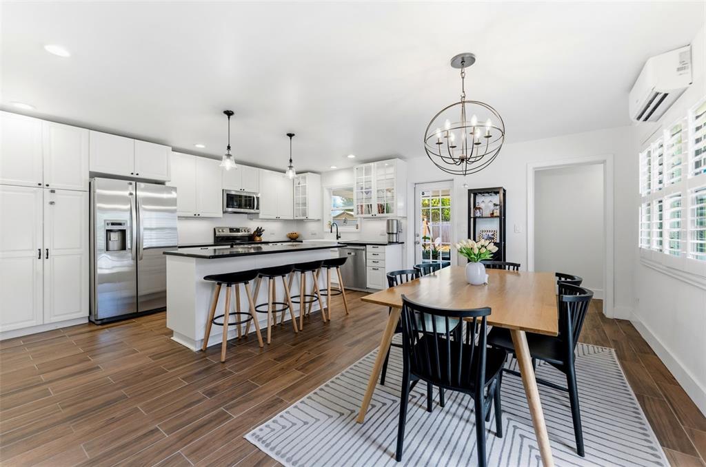A modern kitchen and dining area feature white cabinetry, a center island, and wood-look flooring — 3905 W PEARL AVENUE, TAMPA, FL