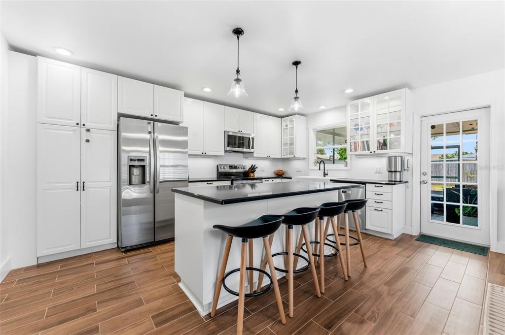 A modern kitchen features white cabinetry, a black-topped island with bar stools, and wood-look flooring — 3905 W PEARL AVENUE, TAMPA, FL