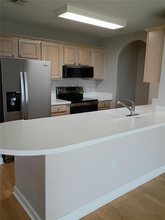 A kitchen features light wood cabinets, stainless steel appliances, and a white peninsula countertop — 750 N TAMIAMI TRAIL UNIT 1007, SARASOTA, FL