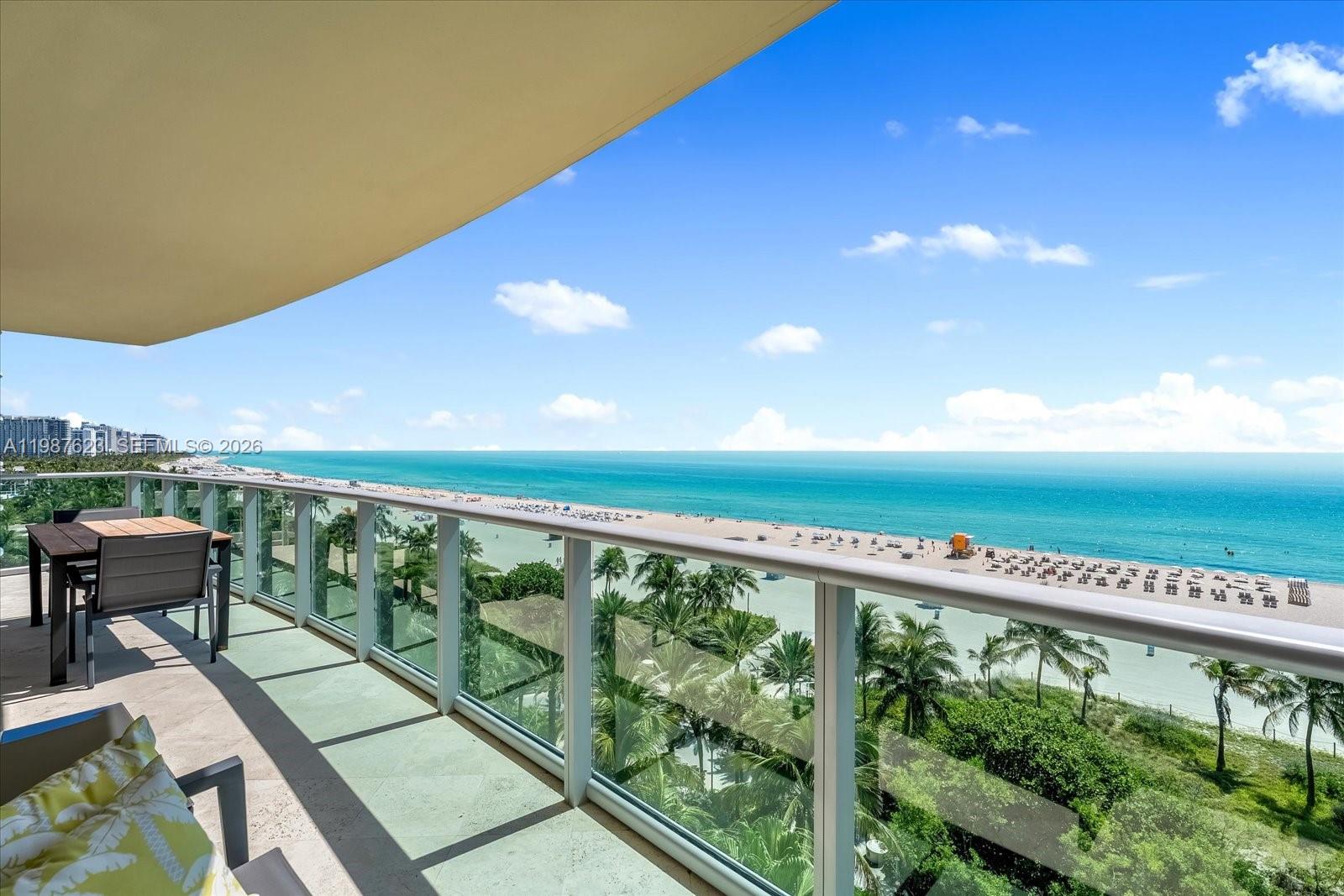 A balcony with a table and chairs overlooks a sandy beach and the ocean — 1455 Ocean Dr # 909, Miami Beach FL 33139, MIAMI BEACH, FL