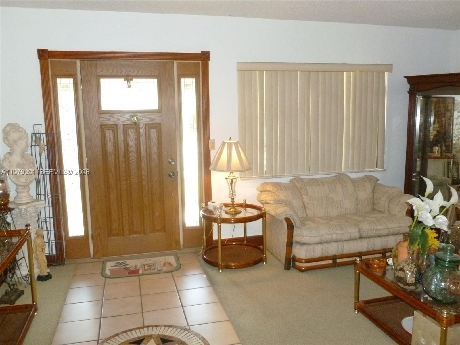 A living room features a wooden front door, tiled entryway, beige carpet, and a sofa — 3261 NW 14th St, Miami FL 33125, MIAMI, FL