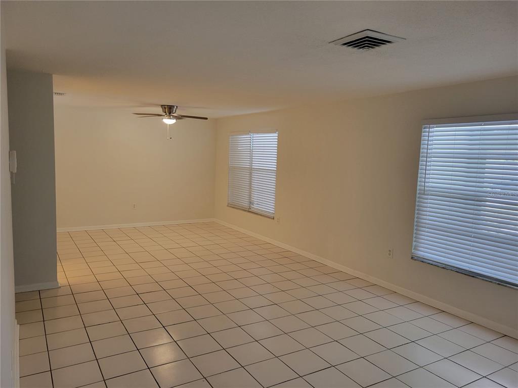 An empty living room features white tile flooring, a ceiling fan, and two windows with blinds — 1508 N SATURN AVENUE, CLEARWATER, FL