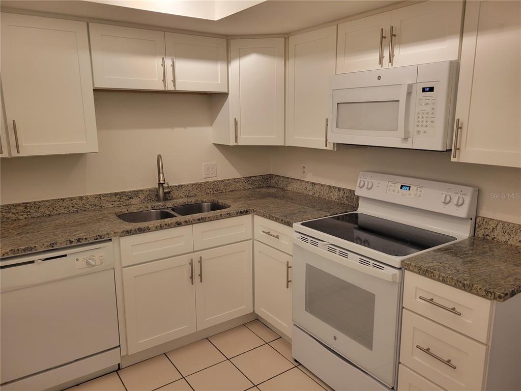 A kitchen features white cabinets, granite countertops, a white oven, and a built-in microwave — 1508 N SATURN AVENUE, CLEARWATER, FL