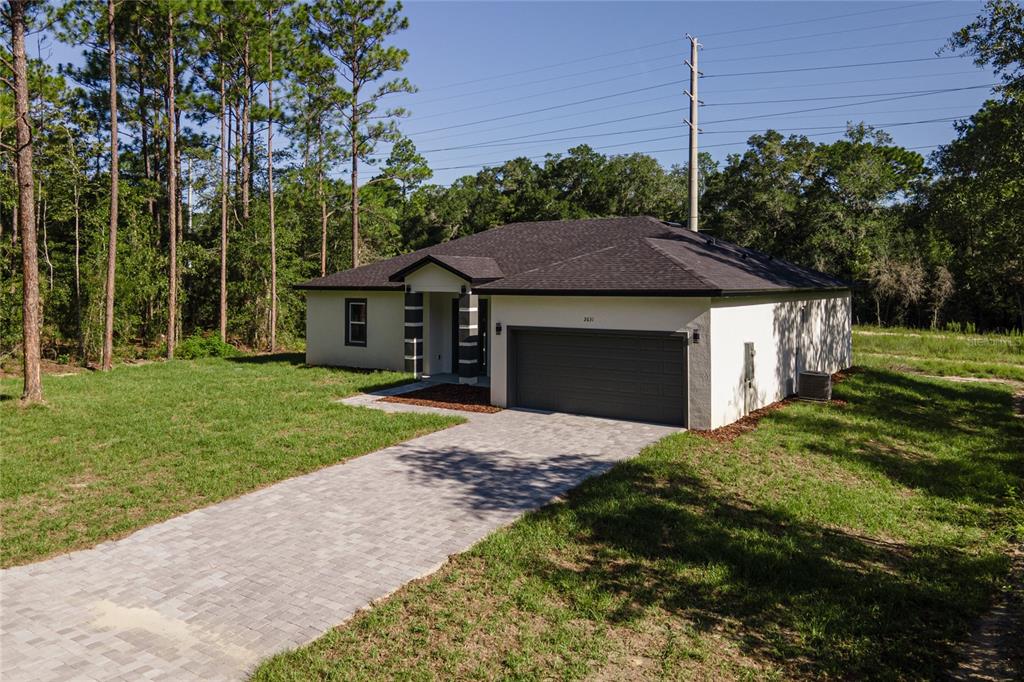 A single-story house with a gray garage door, paved driveway, and surrounding wooded area — 2631 W ROYAL PALM DRIVE, CITRUS SPRINGS, FL