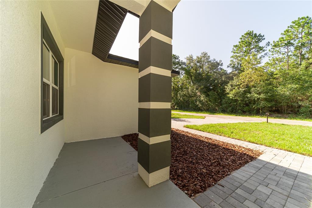 A covered porch features a gray concrete floor, a decorative pillar, and a paver walkway — 2631 W ROYAL PALM DRIVE, CITRUS SPRINGS, FL