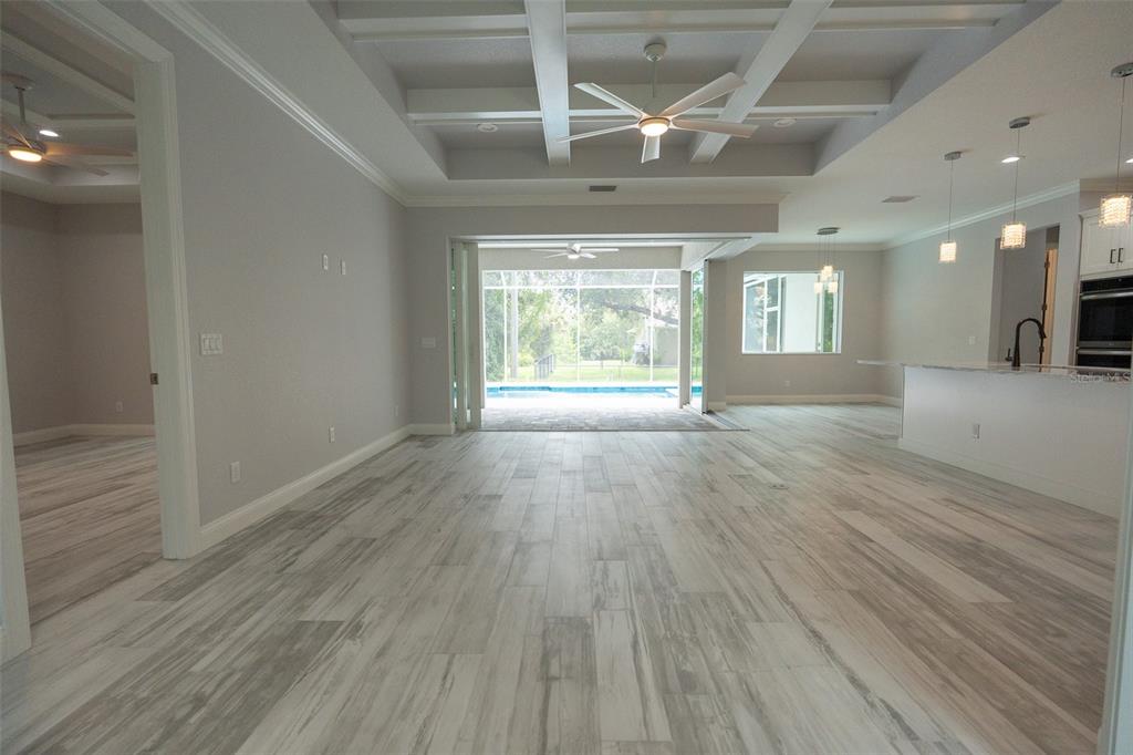 An open-concept living area features light wood-look tile floors, a coffered ceiling, and pool views — 140 SNOWDEN STREET, PORT CHARLOTTE, FL