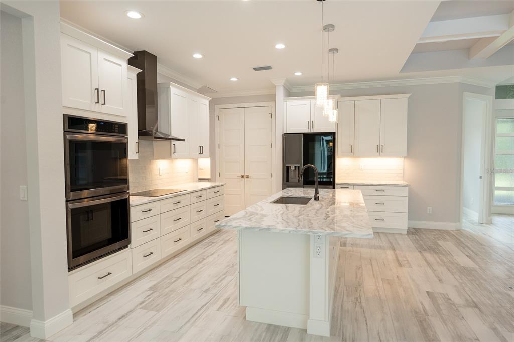 A modern kitchen features white cabinetry, a marble-topped island, stainless steel appliances, and light flooring — 140 SNOWDEN STREET, PORT CHARLOTTE, FL