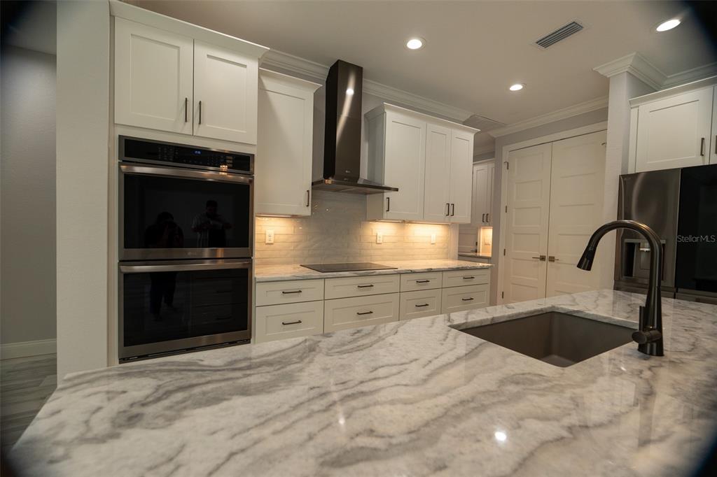 A modern kitchen features white cabinetry, stainless steel appliances, and a marble-topped island with sink — 140 SNOWDEN STREET, PORT CHARLOTTE, FL