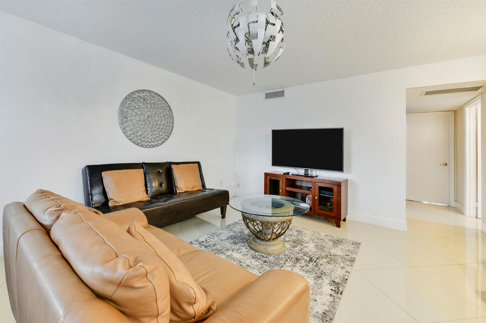 A living room features a tan leather sofa, a black futon, and a glass coffee table — 3100 Springdale Boulevard # 314, Palm Springs FL 33461, PALM SPRINGS, FL