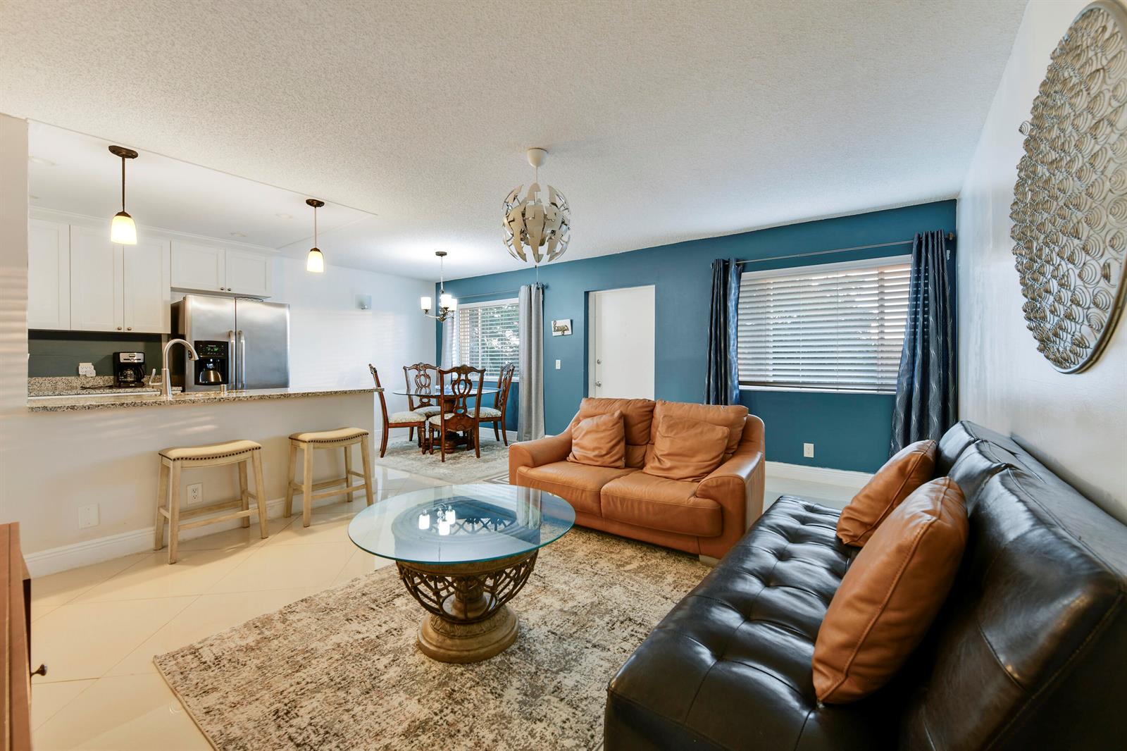 An open-concept living and dining area features a kitchen island, leather sofas, and blue walls — 3100 Springdale Boulevard # 314, Palm Springs FL 33461, PALM SPRINGS, FL