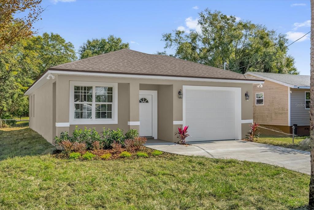 A single-story house with a tan exterior, a white garage door, and a front lawn — 1807 PEACH AVENUE, SANFORD, FL