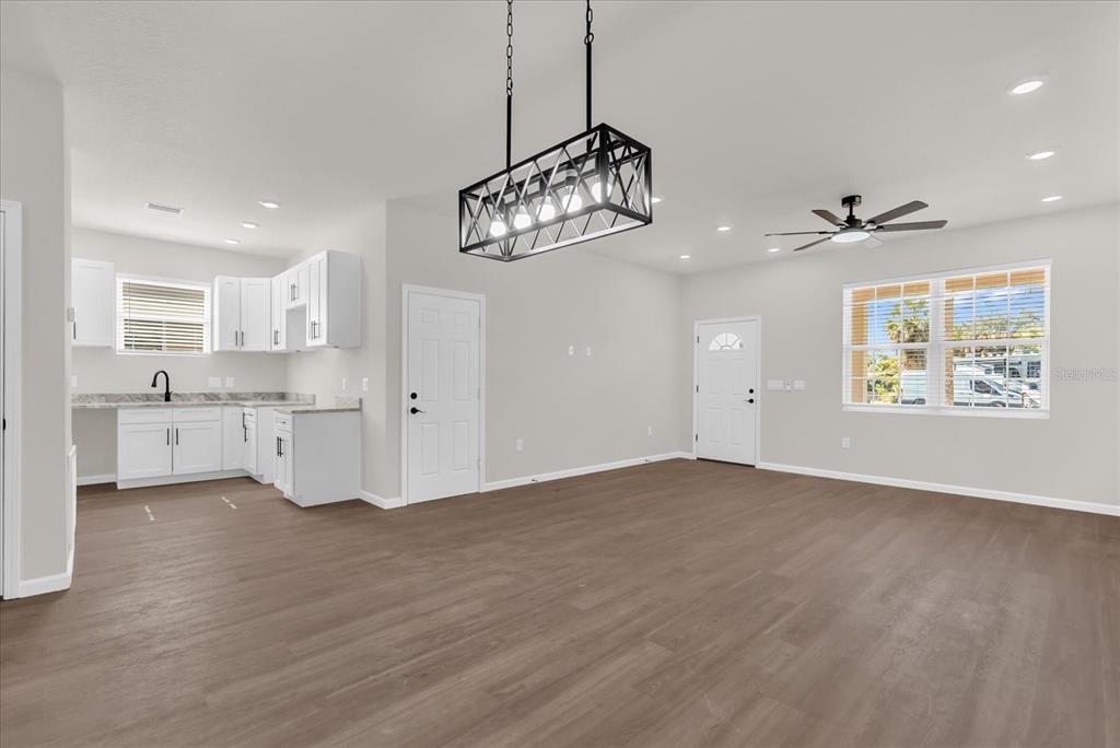 An open-concept kitchen and living area features white cabinets, light wood flooring, and a chandelier — 1807 PEACH AVENUE, SANFORD, FL
