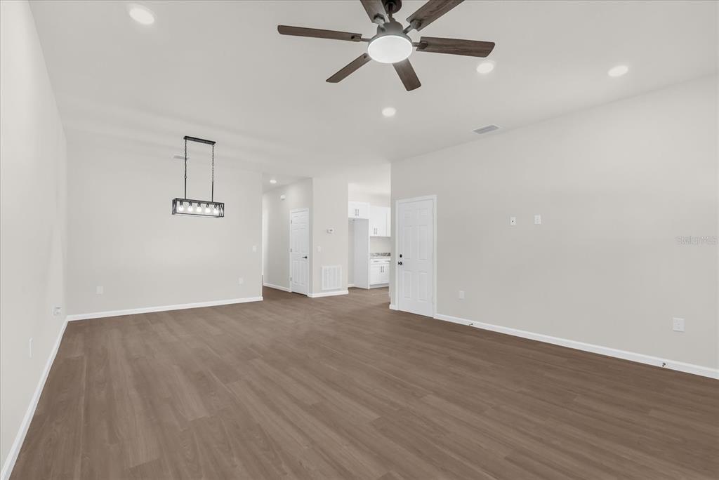 An empty living room features light gray walls, wood-look flooring, a ceiling fan, and a chandelier — 1807 PEACH AVENUE, SANFORD, FL