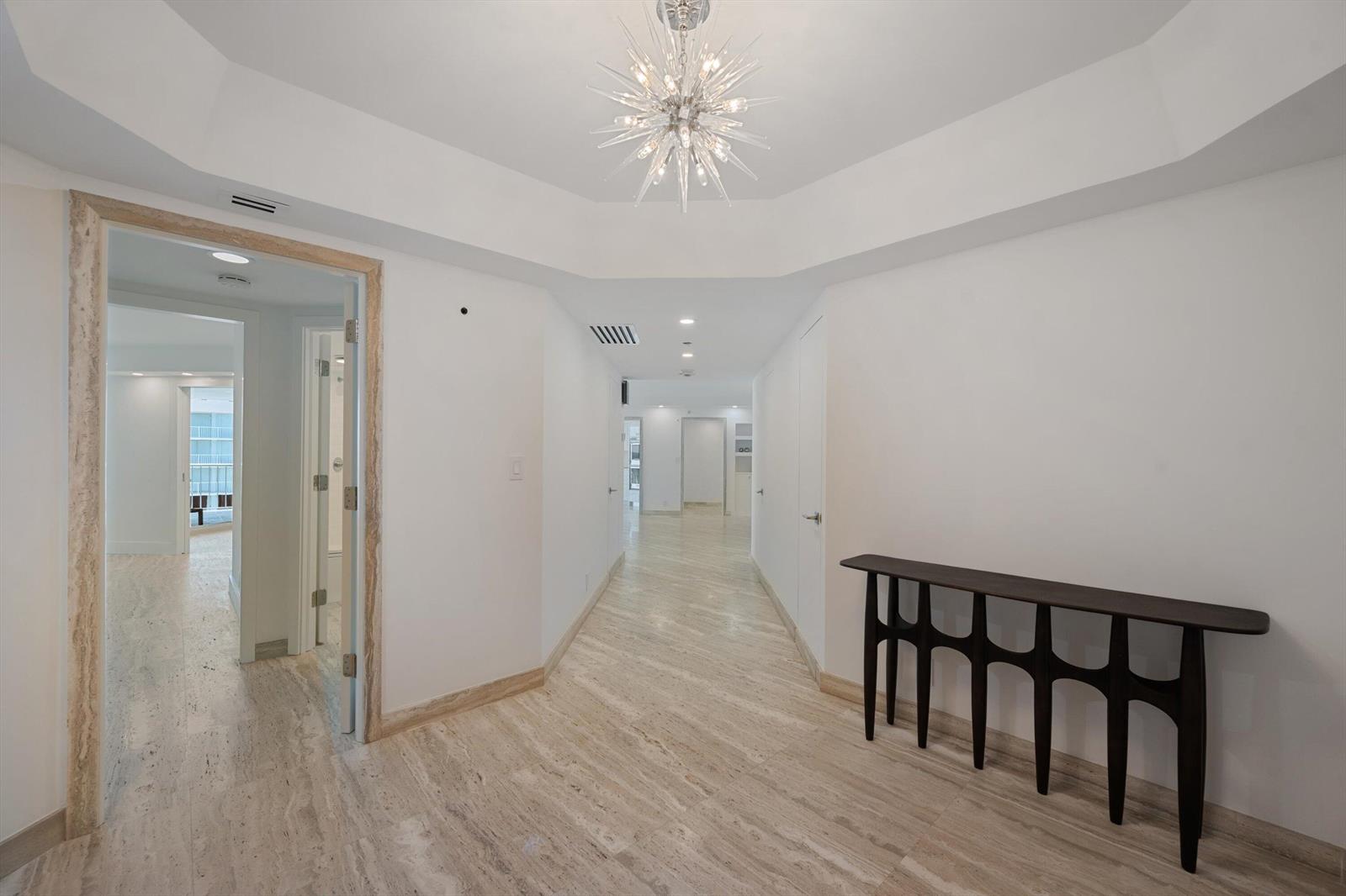 A bright hallway features light stone flooring, white walls, and a modern starburst chandelier — 3170 S Ocean Boulevard # 601n, Palm Beach FL 33480, PALM BEACH, FL