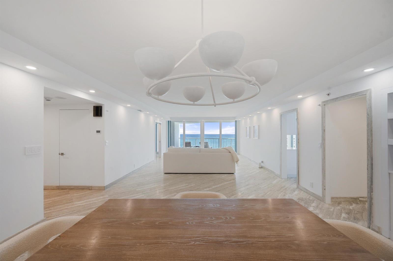A bright, minimalist living and dining area features white walls, wood-look flooring, and ocean views — 3170 S Ocean Boulevard # 601n, Palm Beach FL 33480, PALM BEACH, FL
