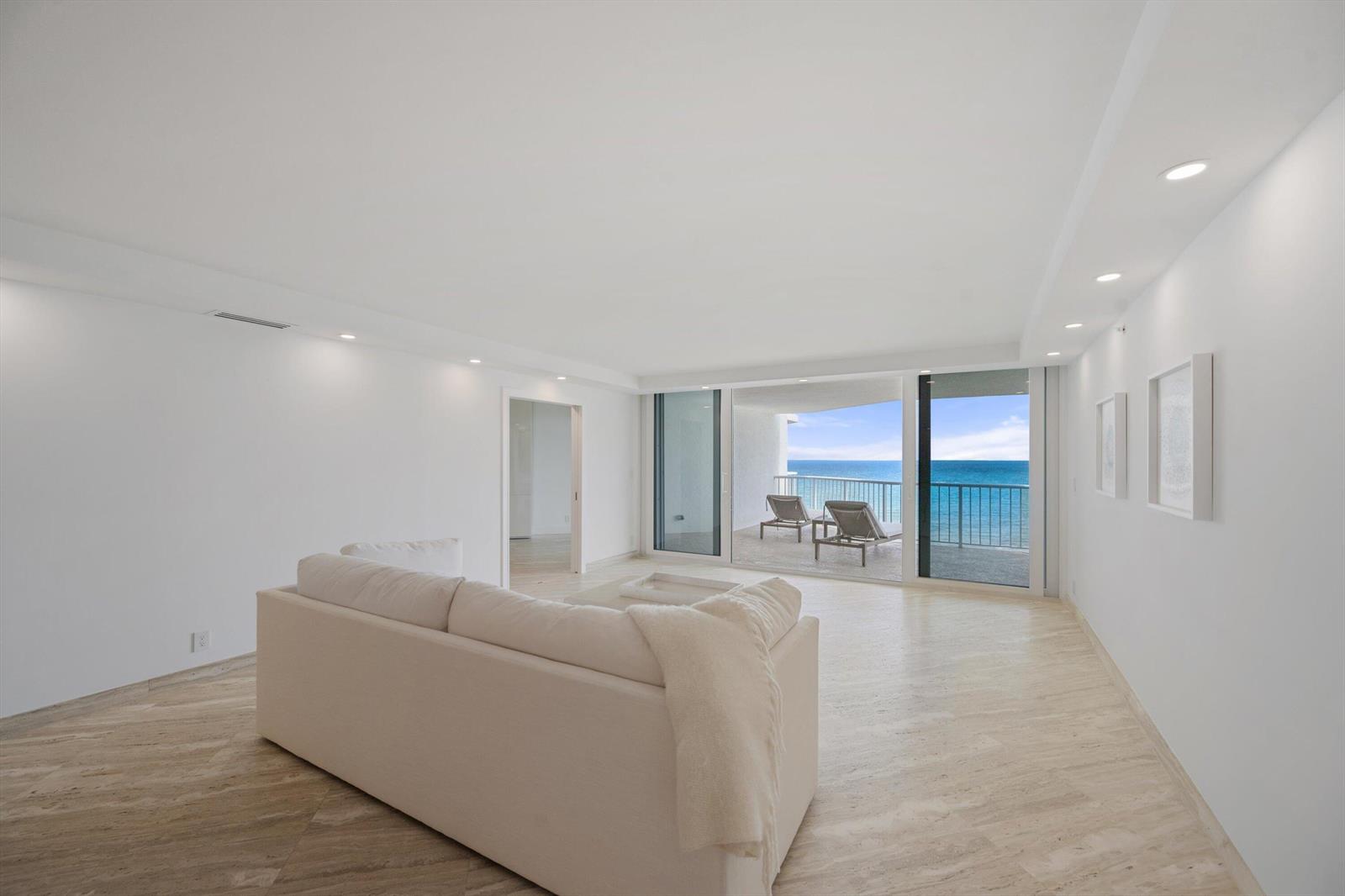 A minimalist living room with white furniture, light tile floors, and a balcony overlooking the ocean — 3170 S Ocean Boulevard # 601n, Palm Beach FL 33480, PALM BEACH, FL