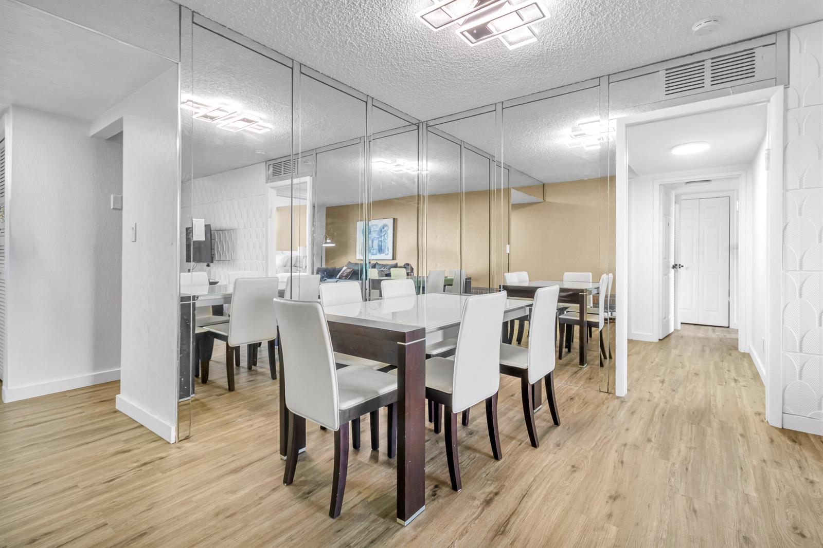 A dining room features a white table, modern chairs, and extensive mirrored wall paneling — 500 Three Islands Boulevard # 109, Hallandale Beach FL 33009, HALLANDALE BEACH, FL