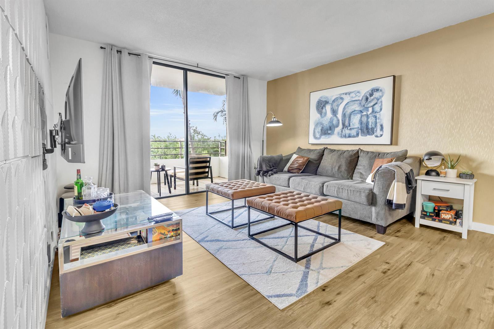 A living room features a grey sofa, two leather ottomans, and a glass coffee table — 500 Three Islands Boulevard # 109, Hallandale Beach FL 33009, HALLANDALE BEACH, FL