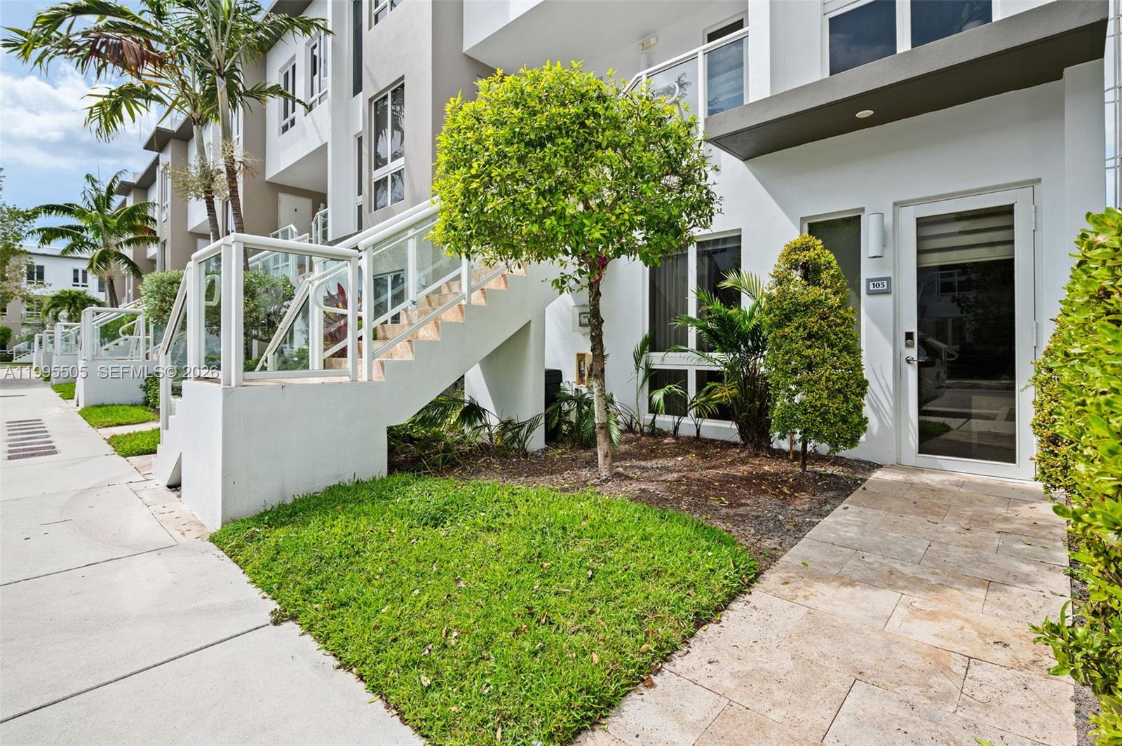 A modern townhouse exterior features a white staircase, a small lawn, and a glass door — 10305 NW 63rd Ter # 105, Doral FL 33178, DORAL, FL