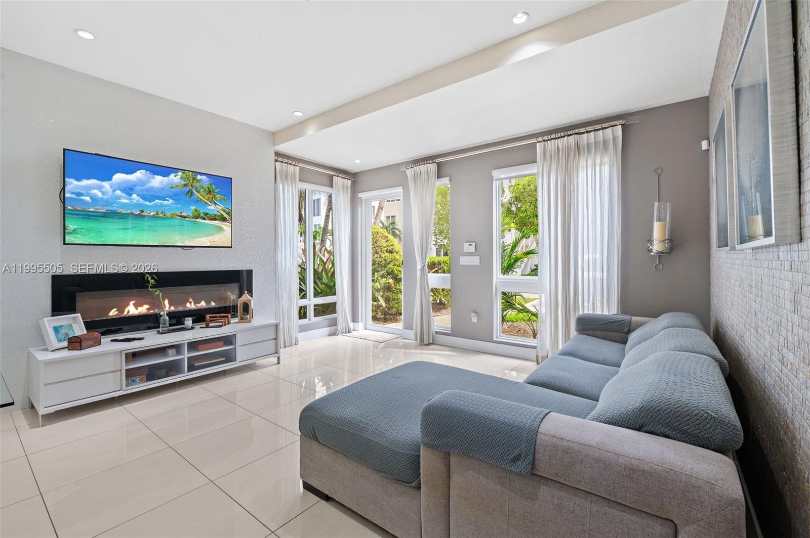 A living room features a wall-mounted television, a linear fireplace, tile flooring, and large windows — 10305 NW 63rd Ter # 105, Doral FL 33178, DORAL, FL