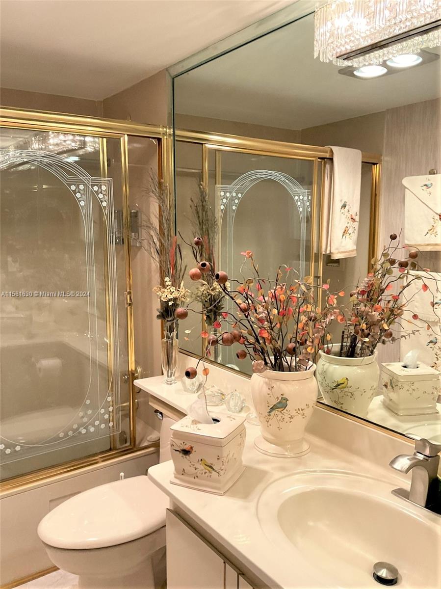 A bathroom features a vanity with a white sink, gold-framed shower doors, and decorative floral accents — 4675 W 18th Ct # 502, Hialeah FL 33012, HIALEAH, FL