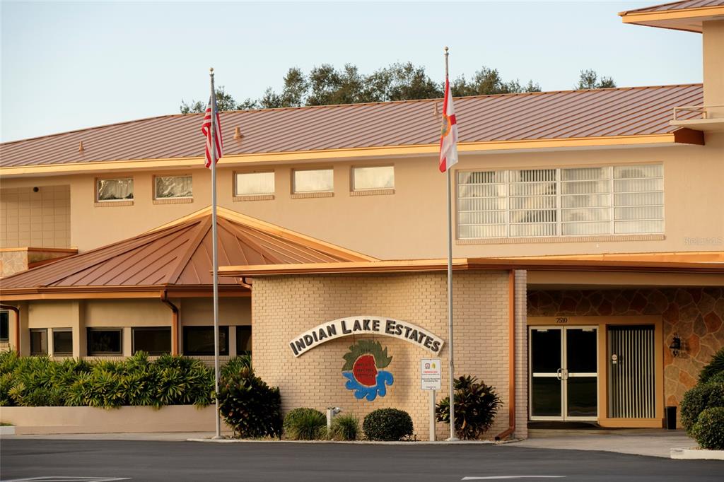 The exterior of a building features a brick facade, a metal roof, and two flagpoles — 1024 GAILLARDIA DRIVE, INDIAN LAKE ESTATES, FL