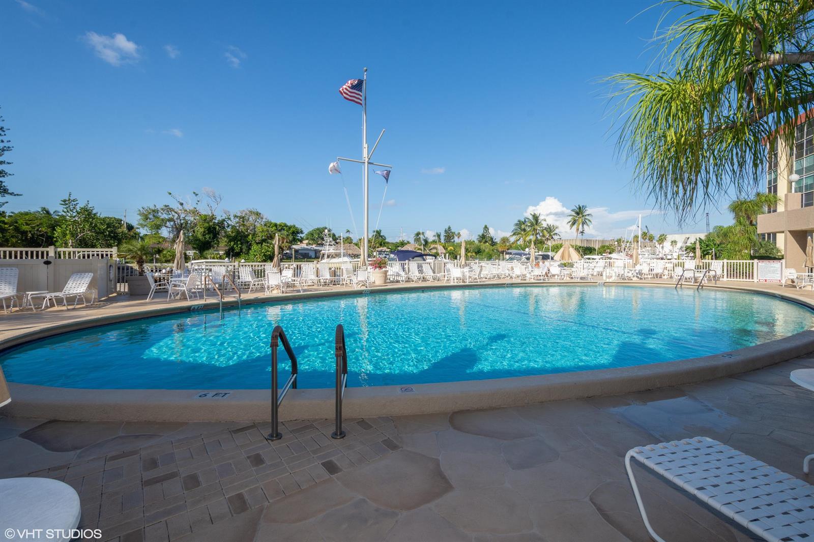 A swimming pool with lounge chairs and a flagpole sits on a sunny patio — 2731 NE 14th St Causeway NE # 103, Pompano Beach FL 33062, POMPANO BEACH, FL