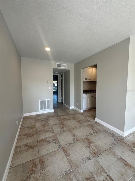 This room features light gray walls, large beige tile flooring, and a view into the kitchen — 24862 US HIGHWAY 19 N UNIT 2105, CLEARWATER, FL