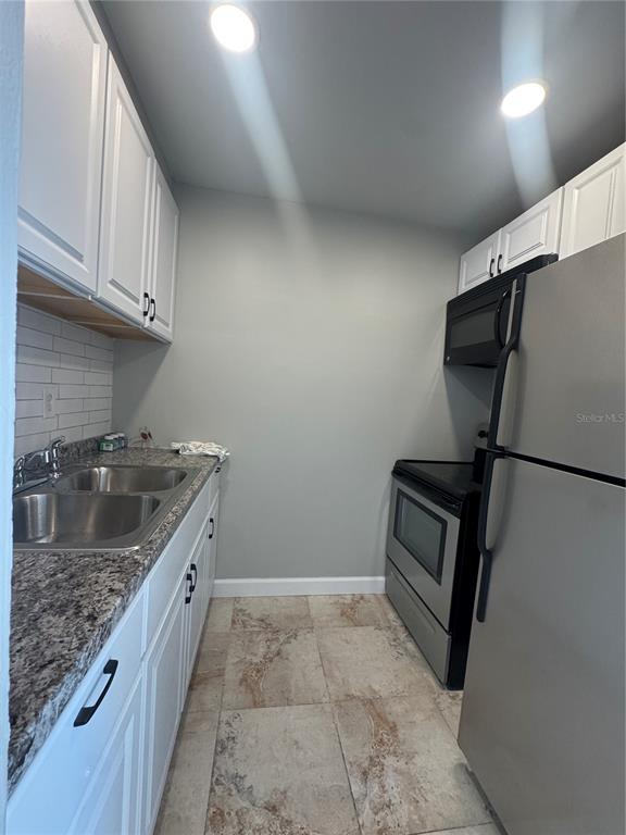 A galley kitchen features white cabinets, granite countertops, stainless steel appliances, and tile flooring — 24862 US HIGHWAY 19 N UNIT 2105, CLEARWATER, FL
