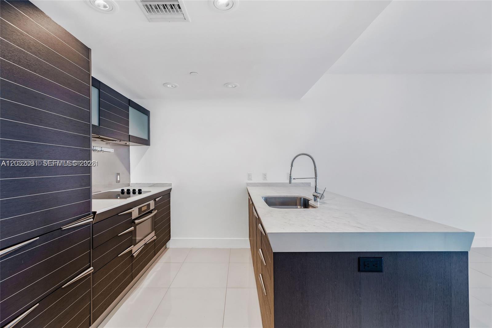 A modern kitchen features dark wood cabinetry, white countertops, and a central island with sink — 200 Biscayne Boulevard Way # 3713, Miami FL 33131, MIAMI, FL