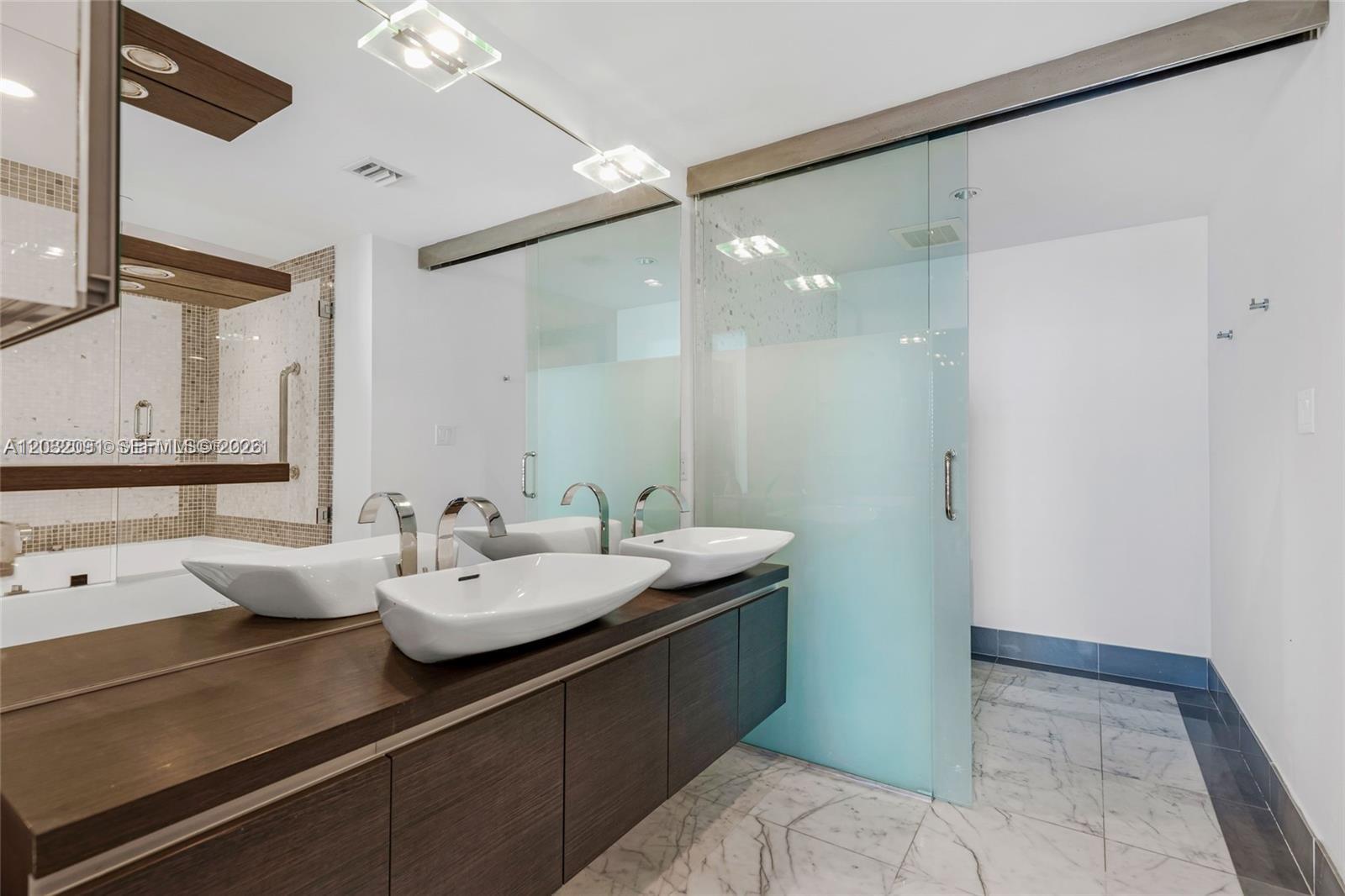 A modern bathroom features a floating wood vanity with dual vessel sinks and glass doors — 200 Biscayne Boulevard Way # 3713, Miami FL 33131, MIAMI, FL