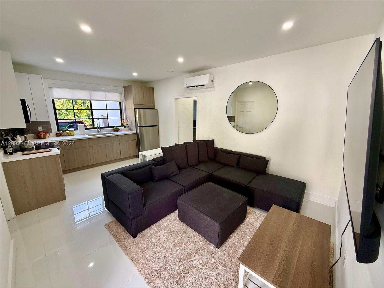 This open-concept living room features a dark sectional sofa, a kitchen, and white tile flooring — 733 Michigan Ave # 9, Miami Beach FL 33139, MIAMI BEACH, FL