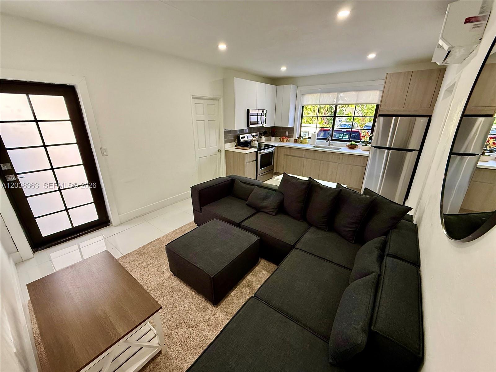 A living room with a dark sectional sofa and ottoman opens into a modern kitchen — 733 Michigan Ave # 9, Miami Beach FL 33139, MIAMI BEACH, FL