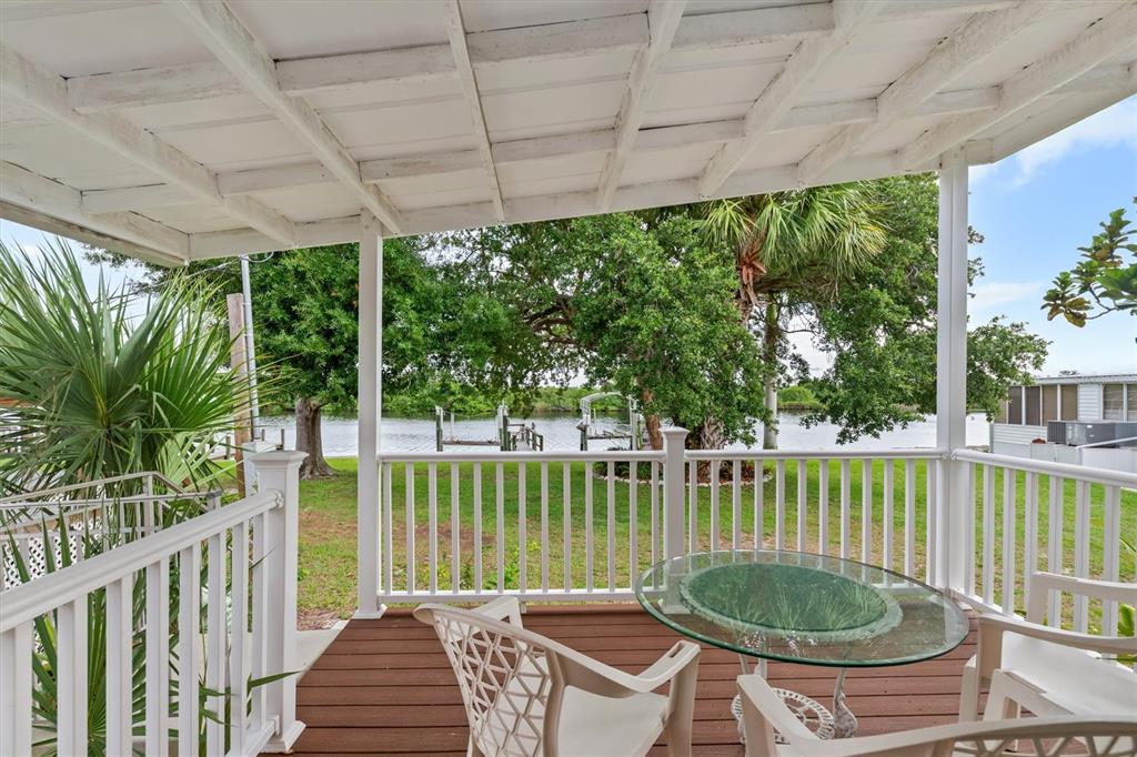 A covered wooden deck features white railings, patio furniture, and a view of a canal — 8320 RIVERSIDE DRIVE UNIT 99, PUNTA GORDA, FL