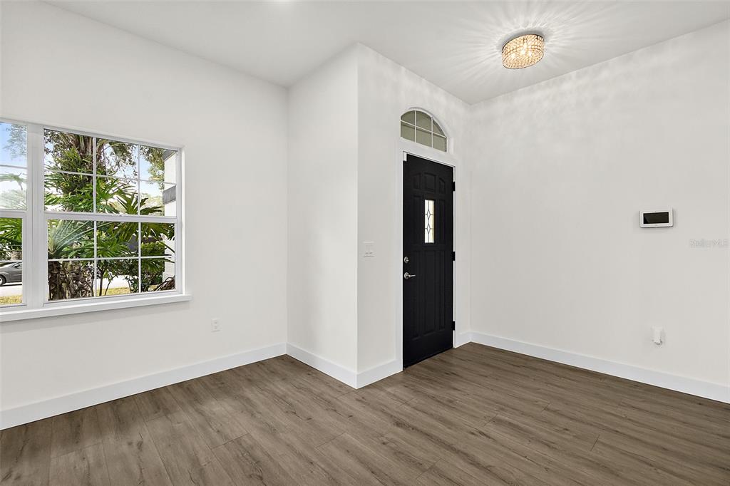 An empty room with wood-look flooring, white walls, a large window, and a black door — 2 SAW MILL COURT, PALM COAST, FL