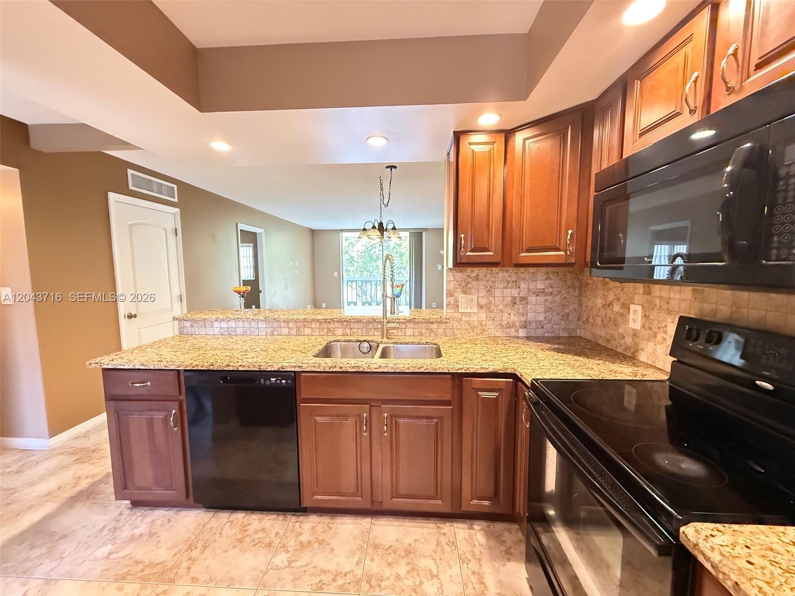A kitchen features wood cabinets, granite countertops, black appliances, and a tiled backsplash — 320 NE 12th Ave # 303, Hallandale Beach FL 33009, HALLANDALE BEACH, FL