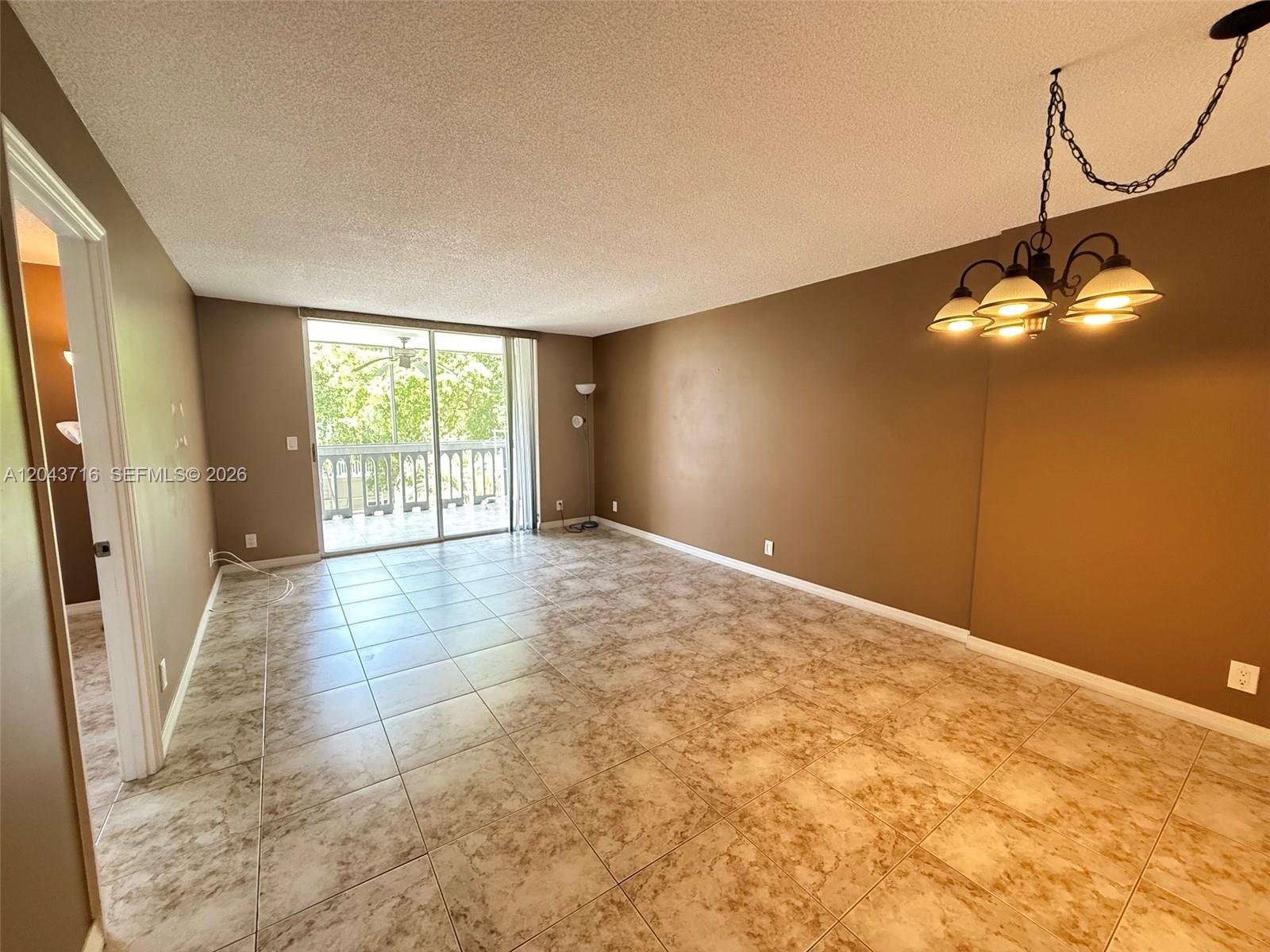 An empty room features brown walls, tiled flooring, a hanging light fixture, and a balcony — 320 NE 12th Ave # 303, Hallandale Beach FL 33009, HALLANDALE BEACH, FL