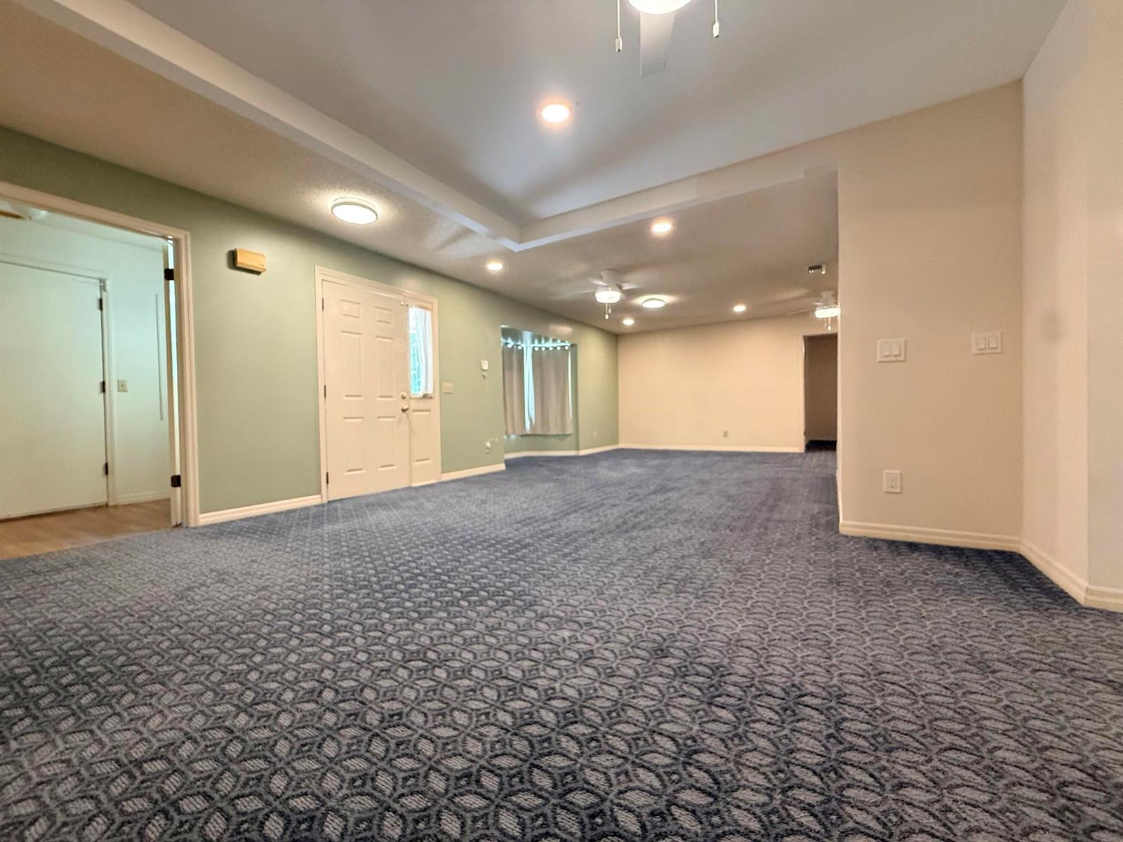 A large, empty room features blue patterned carpeting, light-colored walls, and a tray ceiling — 15647 N 116th Ter Terrace N, FL 33478, FL
