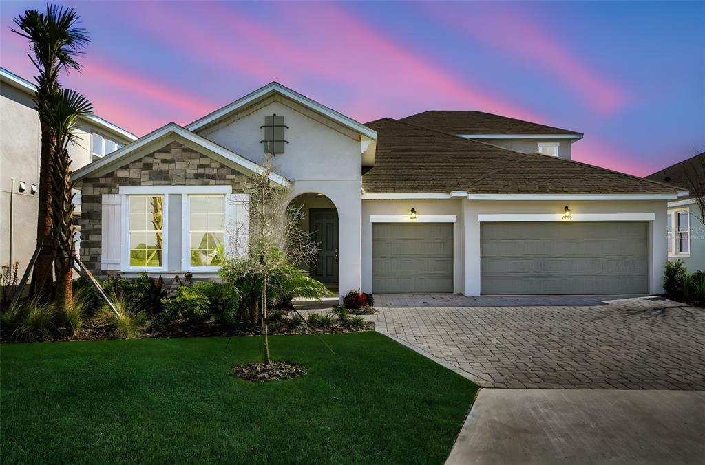 A single-story house with a stone facade, two-car garage, and a paved driveway at dusk — 7425 SEA MANATEE STREET, PARRISH, FL