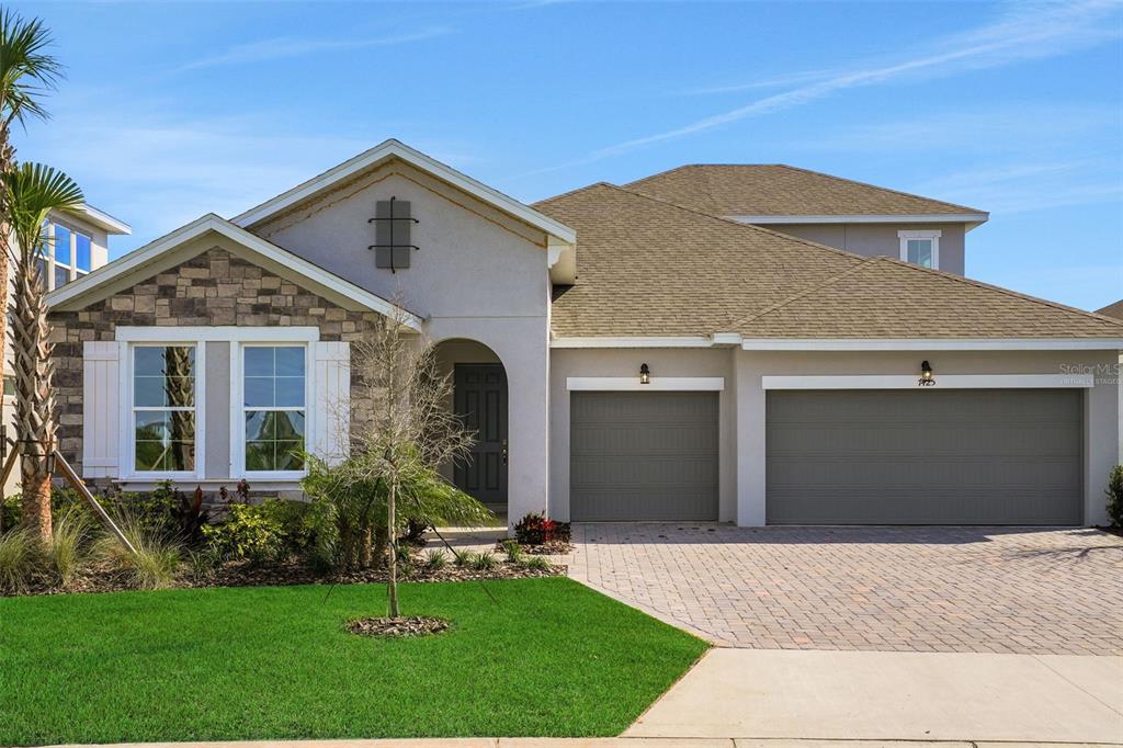 A single-story house with a stone facade, a three-car garage, and a paved driveway — 7425 SEA MANATEE STREET, PARRISH, FL