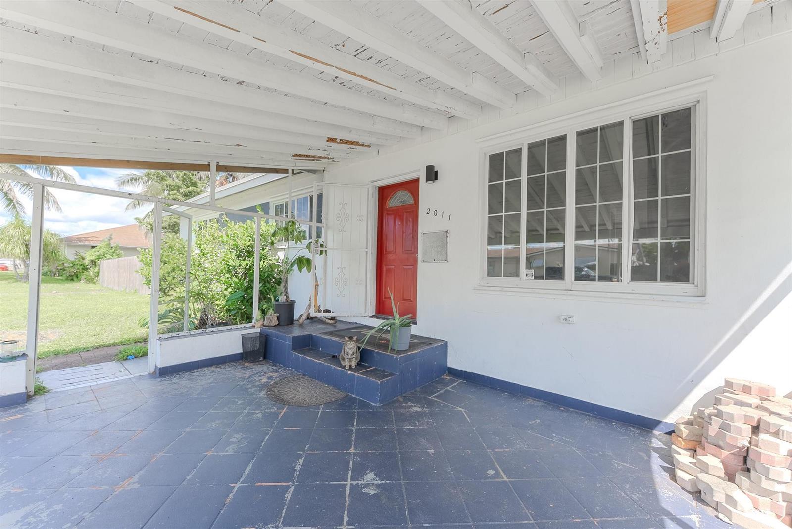 A covered patio features blue tiled flooring, a red front door, and a sitting cat — 2011 SW 97th Terrace, Miramar FL 33025, MIRAMAR, FL