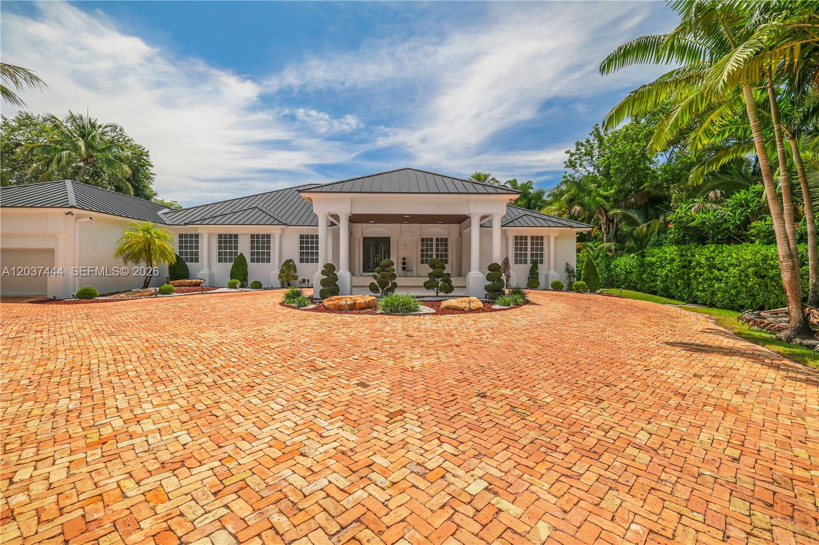 A single-story white house features a dark metal roof and a large brick driveway — 12201 SW 92nd Ave, Miami FL 33176, MIAMI, FL