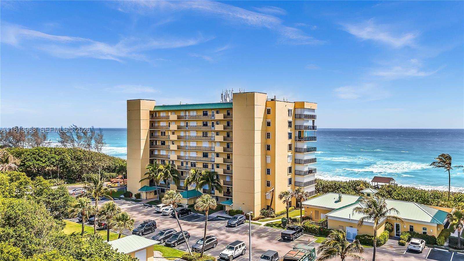 An exterior view of a multi-story yellow apartment building situated next to the ocean — 7370 S Ocean Dr # 815, Jensen Beach FL 34957, JENSEN BEACH, FL