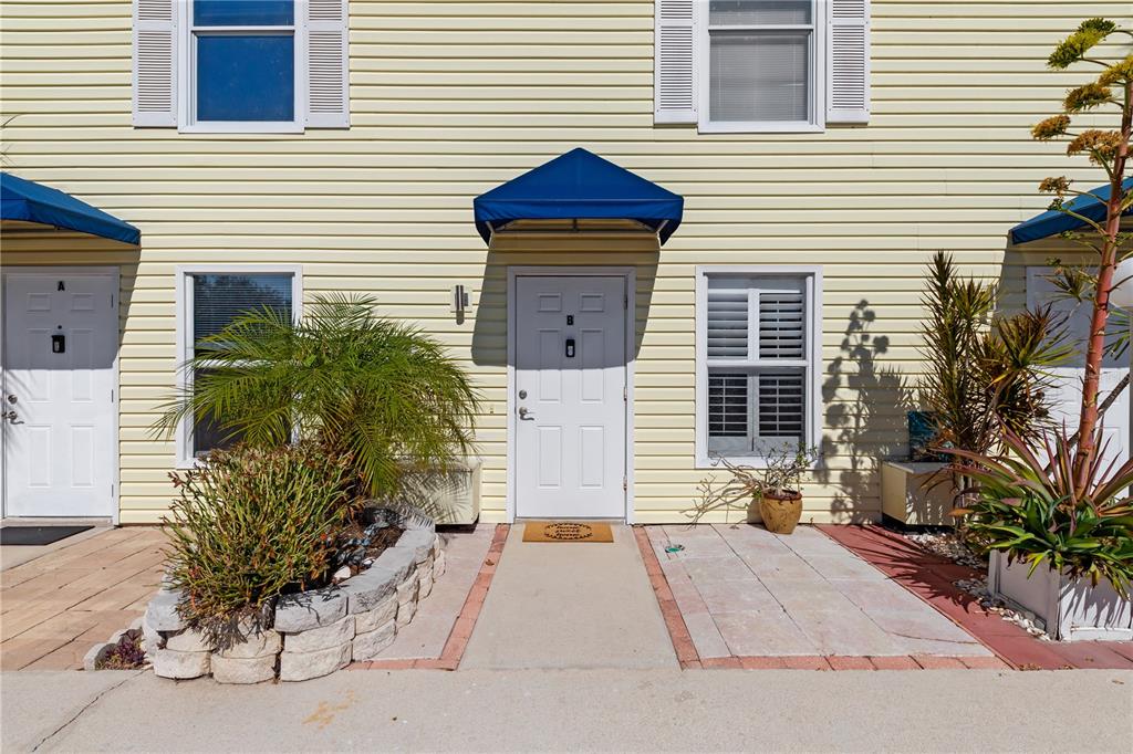 The exterior of a yellow-sided townhouse features a blue awning over a white front door — 26272 RAMPART BOULEVARD UNIT 102, PUNTA GORDA, FL