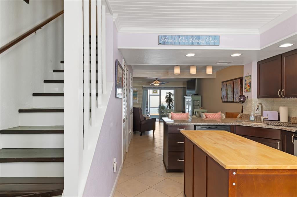 A kitchen with a wooden island and dark cabinets overlooks a living area and stairs — 26272 RAMPART BOULEVARD UNIT 102, PUNTA GORDA, FL
