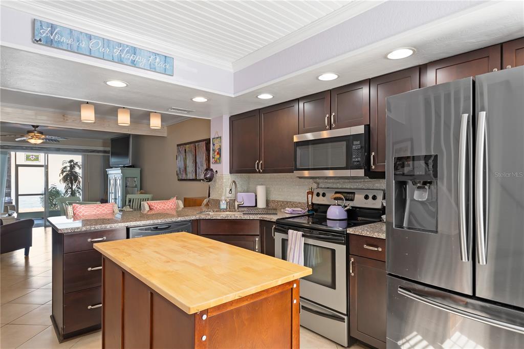 A kitchen with dark wood cabinets, stainless steel appliances, and a wooden kitchen island — 26272 RAMPART BOULEVARD UNIT 102, PUNTA GORDA, FL
