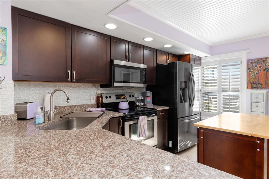 A kitchen features dark wood cabinets, granite countertops, stainless steel appliances, and a center island — 26272 RAMPART BOULEVARD UNIT 102, PUNTA GORDA, FL